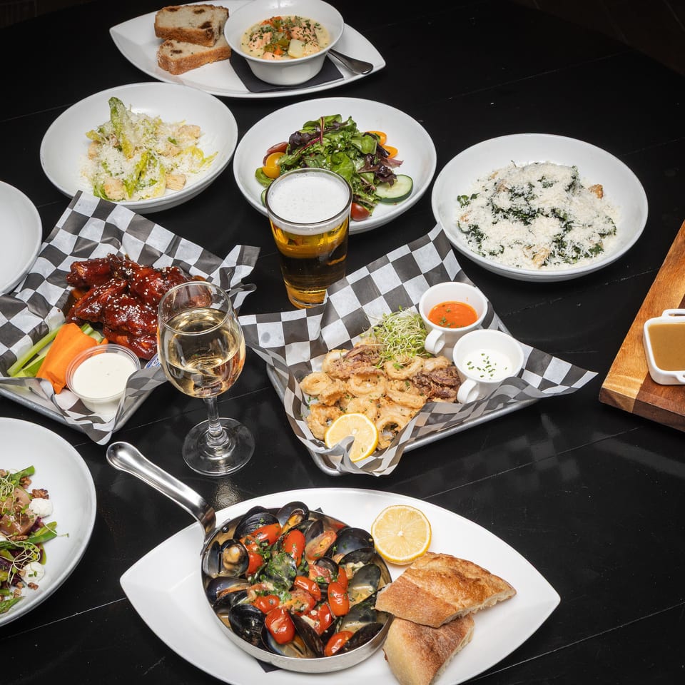 Restaurant table filled with assorted dishes, including mussels, salads, ribs, fried calamari, soup, bread, and drinks.