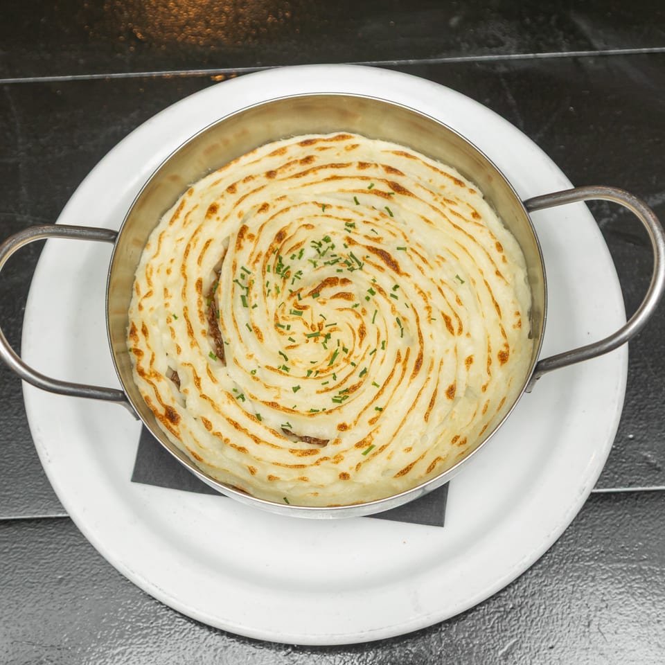 Golden-browned spiral-topped mashed potato casserole garnished with chives in a handled skillet on a white plate.