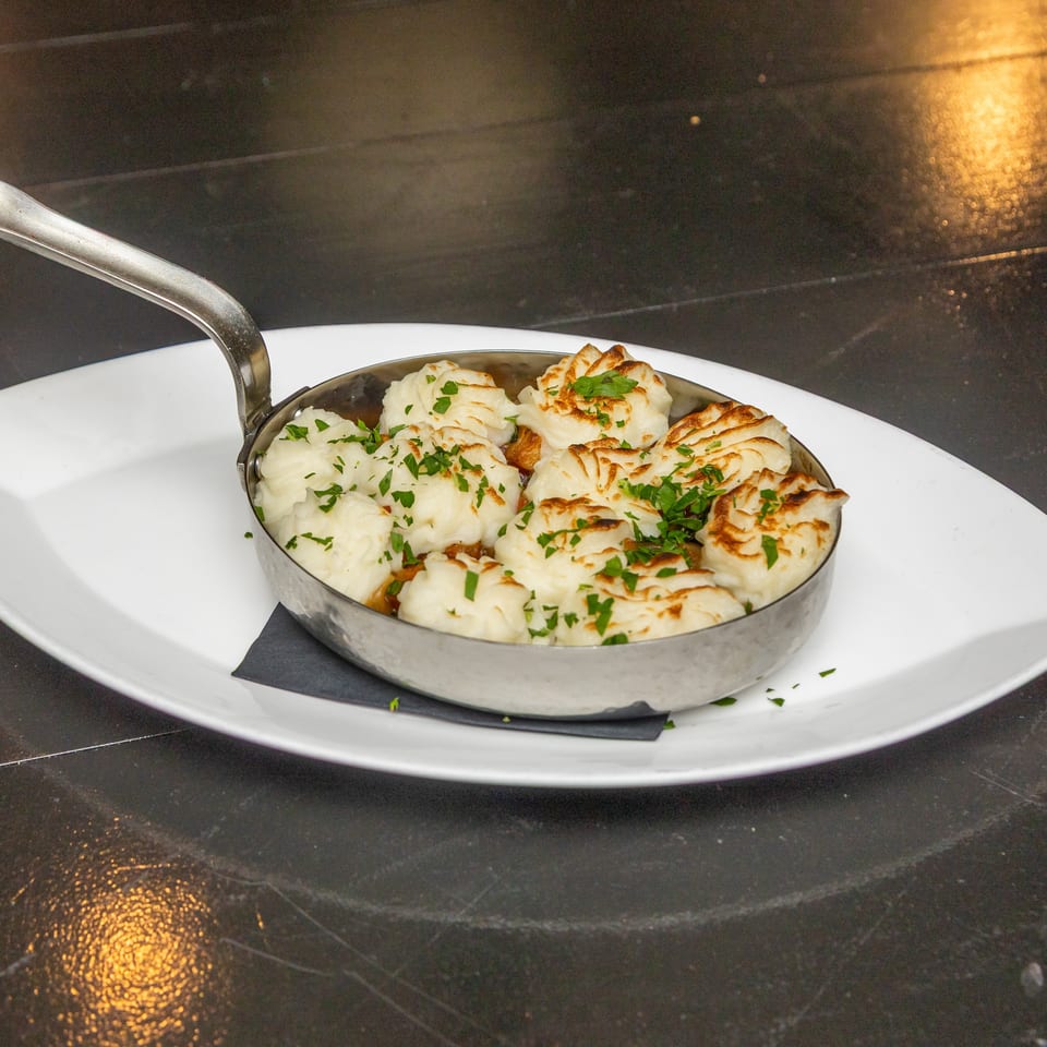 Pan of golden-browned dumplings garnished with chopped parsley, served on a white plate with a spoon.