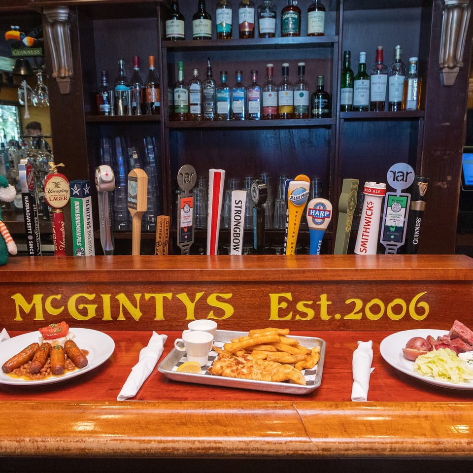 McGinty’s bar displays beer taps, liquor shelves, festive gnomes, and plates of sausages, fish and chips, and corned beef.