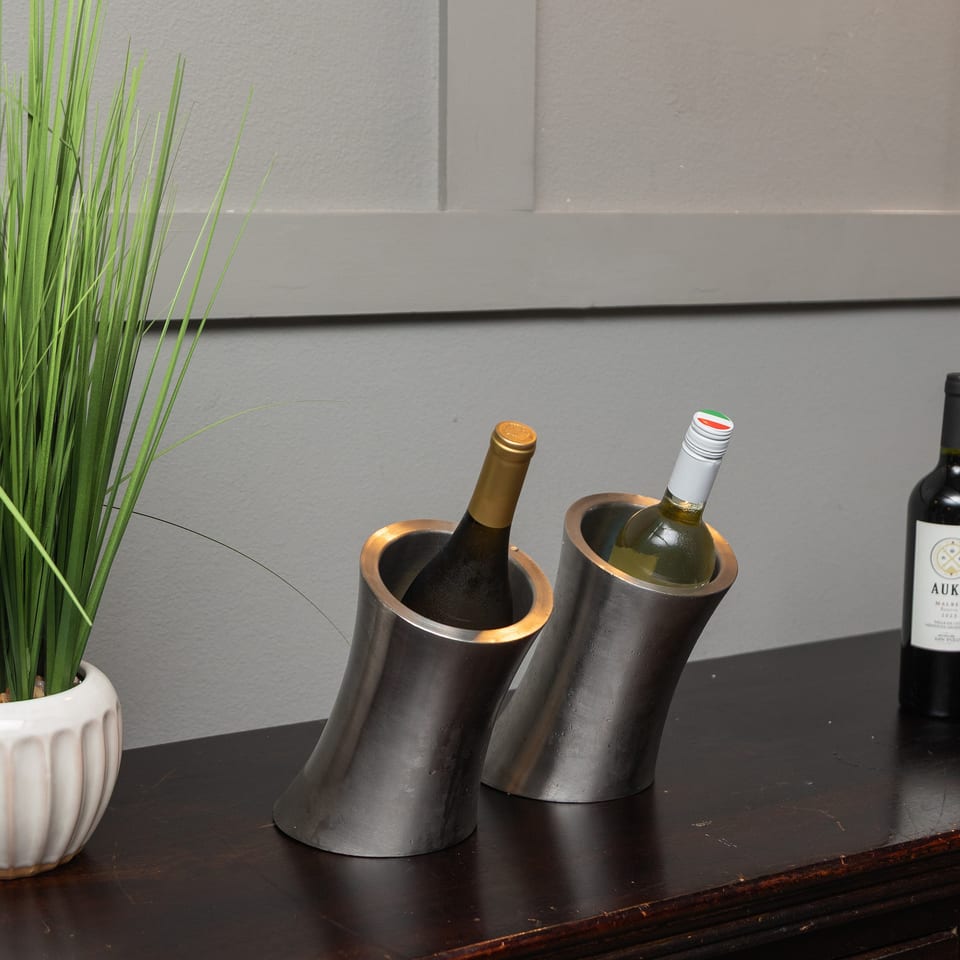 Decorative grass plant, wine bottles in metal coolers, and additional wine bottles displayed on a dark wooden restaurant counter.