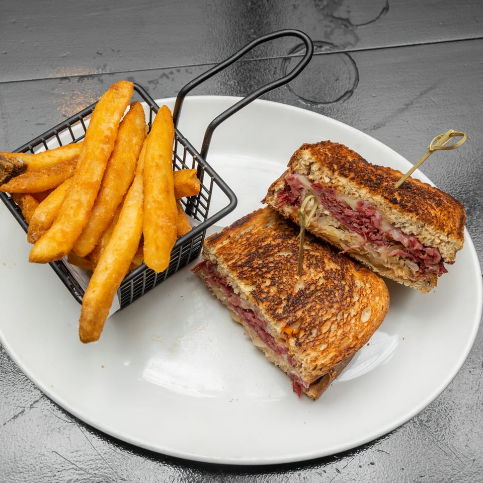 Grilled corned beef and Swiss sandwiches with sauerkraut served alongside golden fries on a white plate.