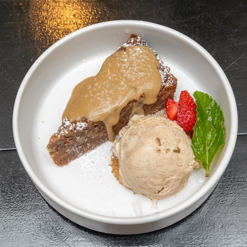 Chocolate dessert topped with caramel sauce and powdered sugar, served with ice cream, strawberries, and mint.