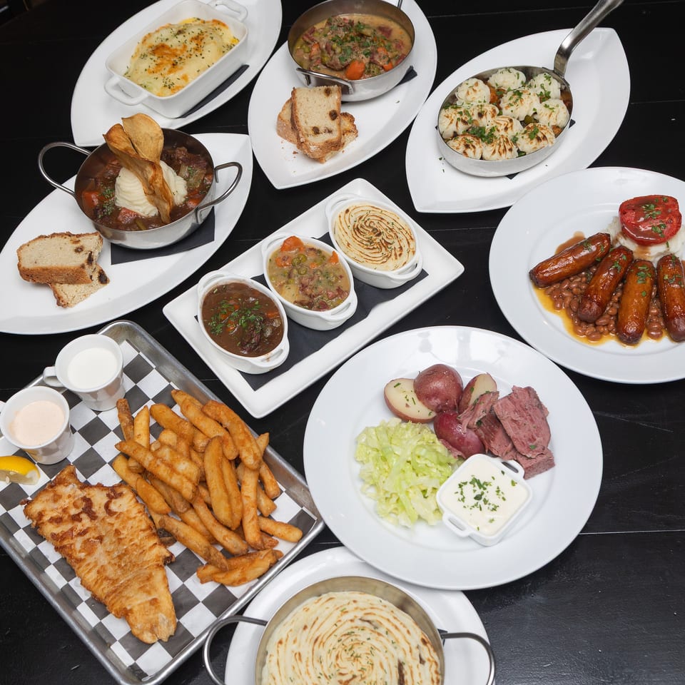 Overhead view of a restaurant spread featuring meat dishes, sausages, mashed potatoes, casseroles, vegetables, bread, and fries.