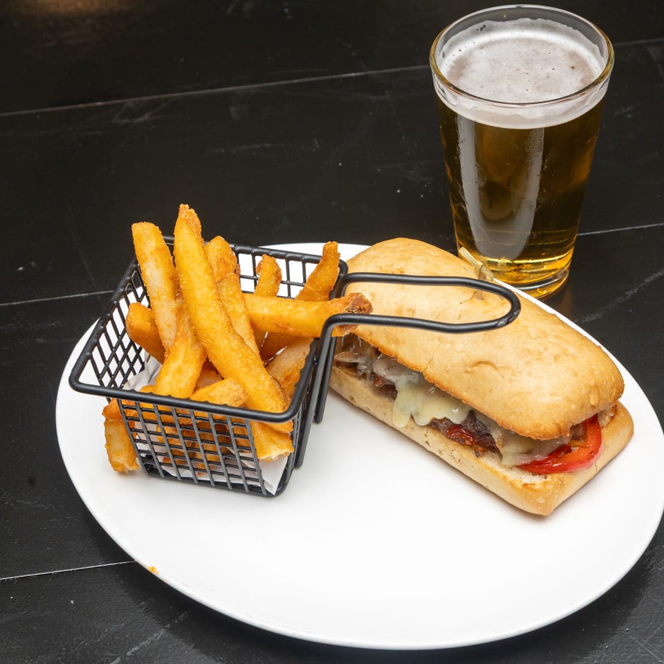 Cheeseburger with tomatoes and melted cheese, served with fries and a foamy beer on a white plate.