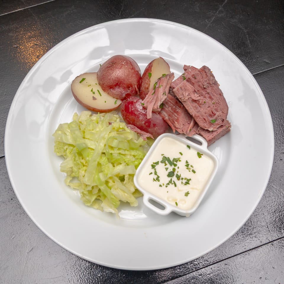 Plate of sliced corned beef, red potatoes, cabbage, and creamy herb sauce on a white dish.
