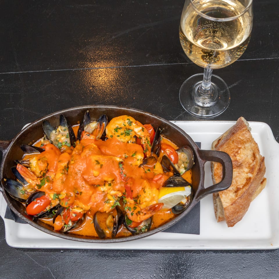 Seafood stew with shrimp, mussels, tomatoes, herbs, and lemon in a cast-iron skillet, served with toasted bread and white wine.