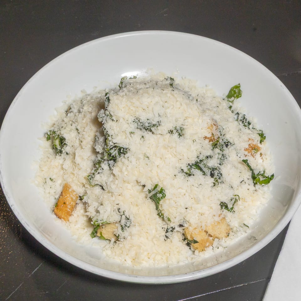 White plate of shredded coconut-covered food garnished with green herbs and peppers on a dark restaurant table.