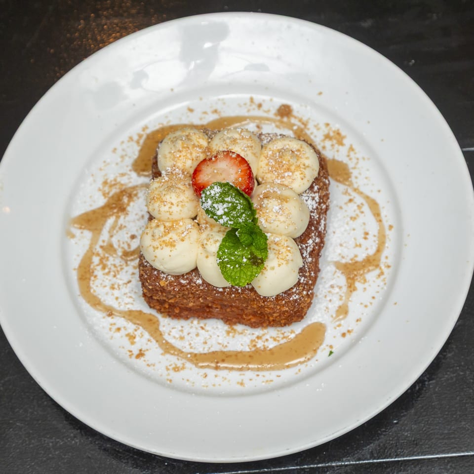 Dessert topped with whipped cream, strawberry, mint, powdered sugar, and crumble on a white plate.
