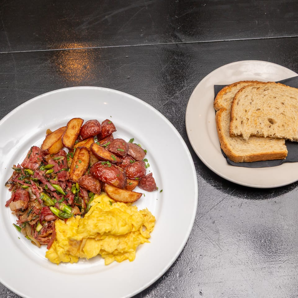 Breakfast plate with scrambled eggs, roasted potatoes, sautéed meat and vegetables, alongside slices of multigrain toast.