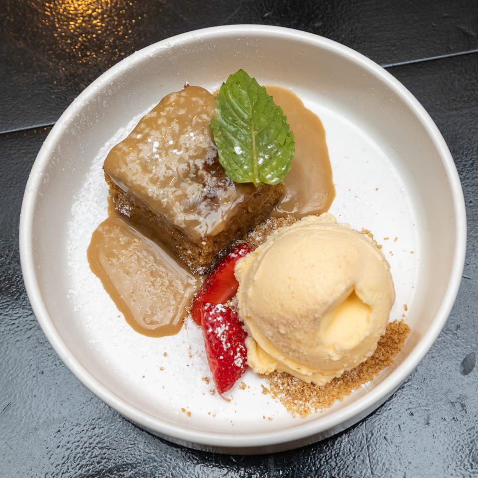 Chocolate cake topped with caramel sauce and mint, served with vanilla ice cream, strawberries, powdered sugar, and crumb garnish.